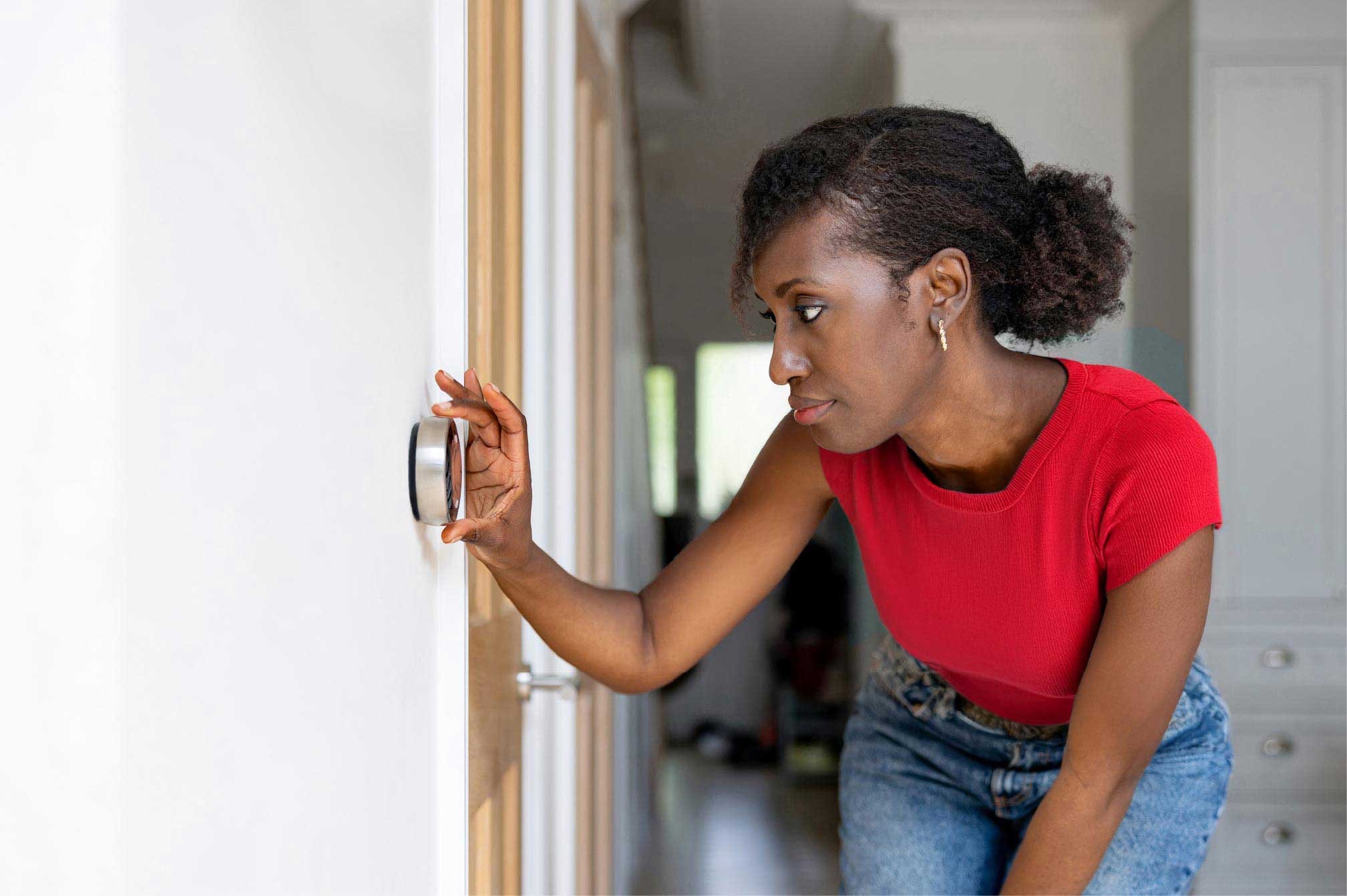 A woman in a red t-shirt turning down the thermostat in her home.